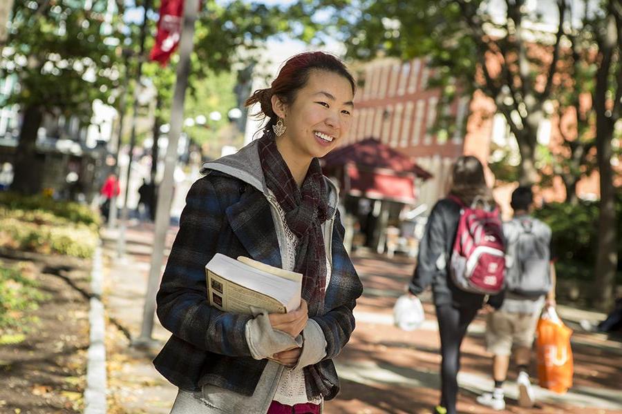 学生拿着书站在大学校园的小路上